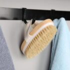 A body brush with a strap hangs on a hook between two towels.
