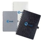 Three spiral-bound notebooks are displayed. The covers have a textured design and come in white, gray, and black. Each notebook has a band with a blue C track logo on it.