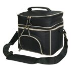 A black, insulated cooler bag with tan accents. It features a top handle, a detachable shoulder strap, dual zippers on the main compartment, and a smaller front zip pocket. The bag has a rectangular shape and a soft, fabric exterior.