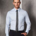 A man with short hair is wearing a light blue striped dress shirt and a dark tie, standing against a textured gray wall. He has one hand in his pocket and wears a black belt.