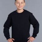 A young boy with short hair smiles confidently, wearing a plain black crewneck sweatshirt and dark pants. He stands against a simple gray background with his hands on his hips.
