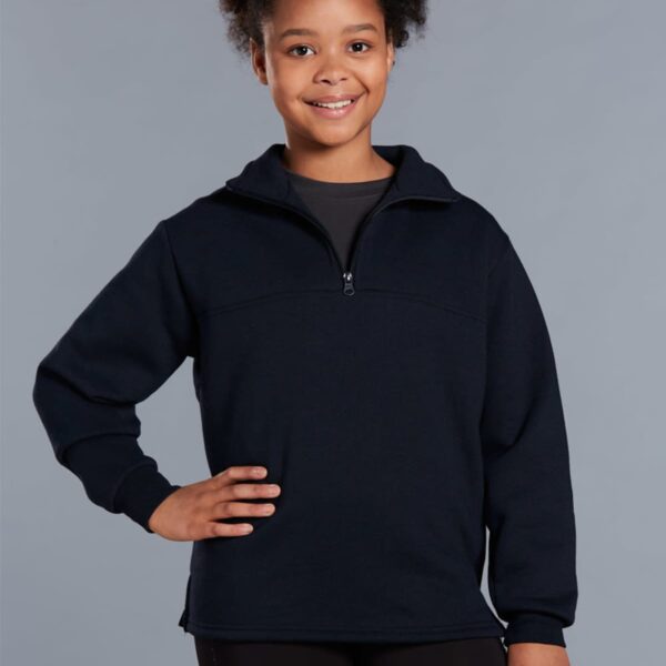 A smiling person wearing a navy blue zip-up sweater and black pants stands with one hand on their hip against a plain gray background.