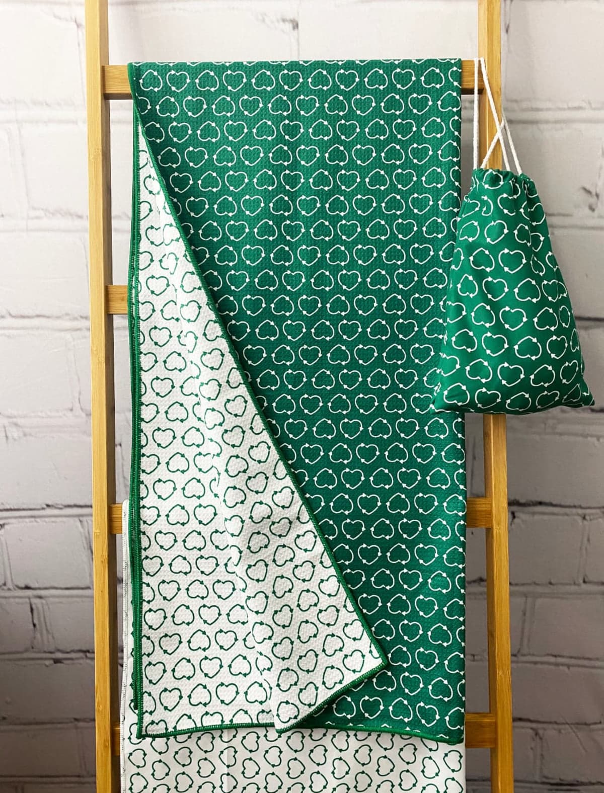 A green fabric with white cloud patterns is draped over a wooden ladder. Beside it, a matching drawstring bag hangs. The ladder is set against a white brick wall.