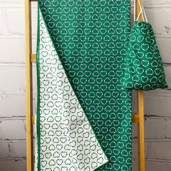 A green and white patterned quilt featuring cloud motifs is draped over a wooden ladder. A matching drawstring bag hangs beside it. The background is a white brick wall.