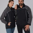 A woman and a man are posing together, both wearing matching black jackets with gray sleeves and white piping. The woman has one arm resting on the mans shoulder. She is wearing jeans, while the man is in black pants. They stand against a plain background.