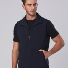 A man poses wearing a dark blue zip-up fleece vest over a black T-shirt. He stands with one hand in his pocket against a plain gray background.