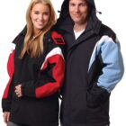 A smiling woman and man stand side by side wearing winter jackets. The woman has a black jacket with red and white sleeves, while the man wears a black jacket with light blue and white sleeves and a hood.
