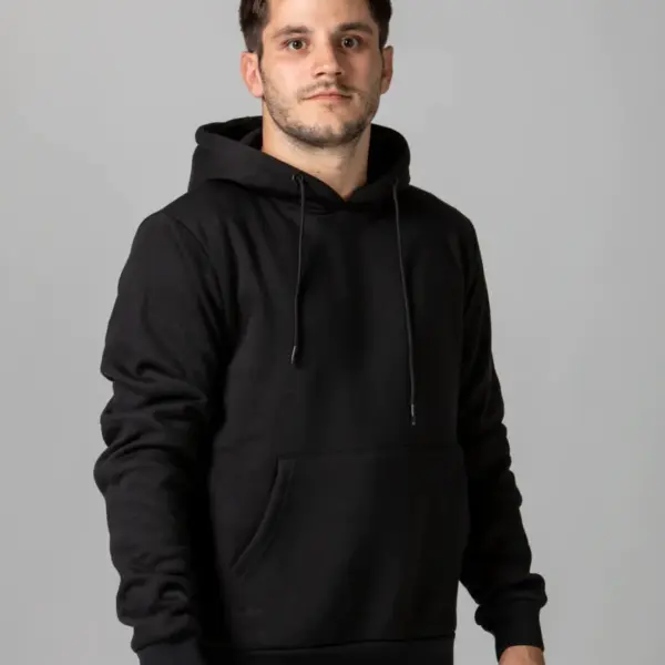 A man wearing a black hoodie and gray pants stands against a plain gray background. The hoodie has a front pocket and drawstrings. He is looking directly at the camera with a neutral expression.