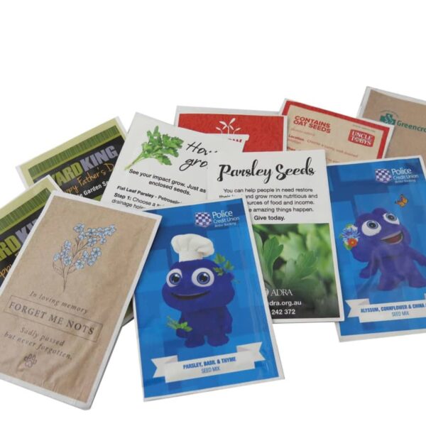 A collection of colorful seed packets arranged on a white surface. Varieties include forget-me-nots, parsley, basil, thyme, and more. Some packets feature playful designs with cartoon characters, while others have illustrations of plants.