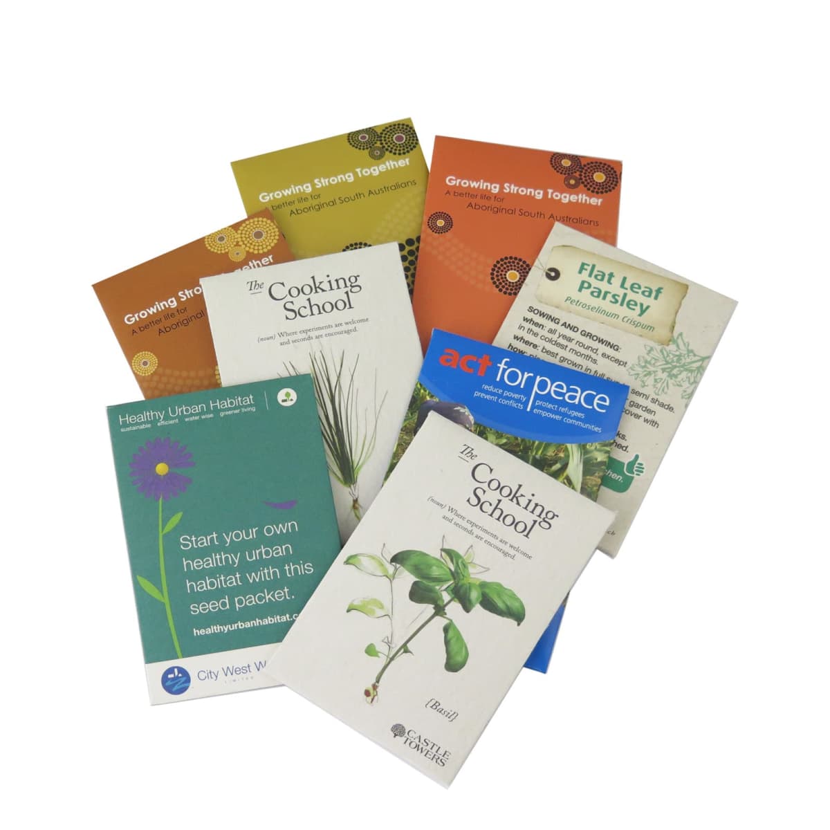 A collection of colorful brochures is fanned out in a semi-circle. They feature gardening and cooking themes, with titles such as The Cooking School, Growing Strong Together, and Flat Leaf Parsley.