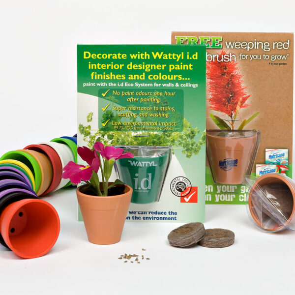 A colorful set featuring small plant pots, a packet of seeds, soil discs, and a plant in a pot. A promotional card for Wattyl i.d paint and a brush for weeping red are included, emphasizing eco-friendliness and interior design ideas.