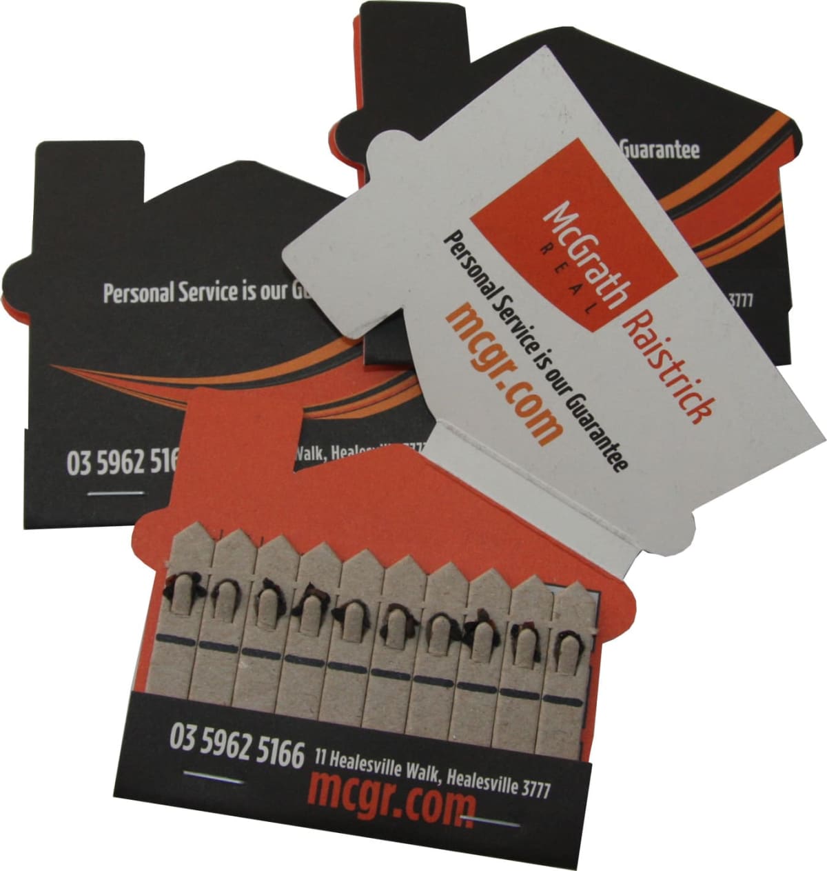 Two business card designs in the shape of a house, one mostly black with orange accents, and another orange with black accents. Both feature contact information and branding for McGrath Ralstrick, emphasizing personal service as a guarantee.