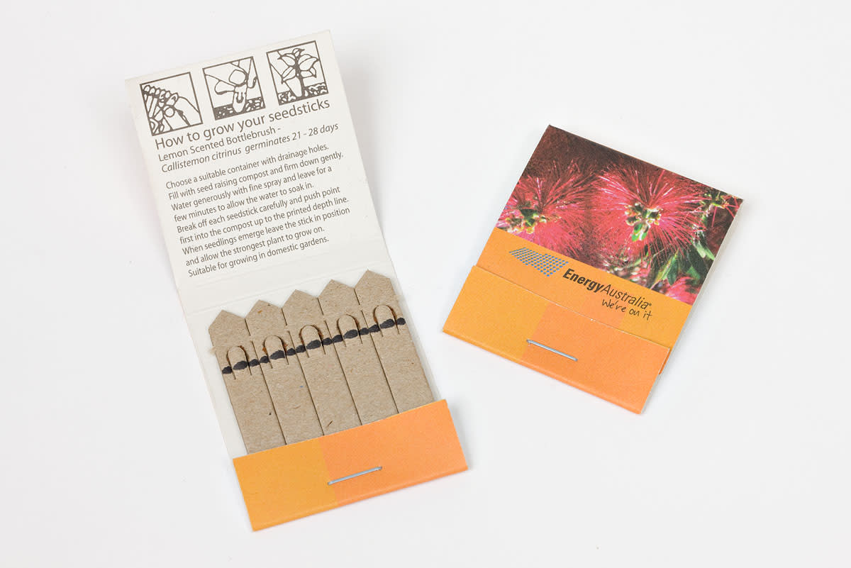 Open and closed matchbook-style seed packets, labeled EnergyAustralia. The open packet shows labeled planting sticks and instructions for growing seeds, with images of flowers on the cover.