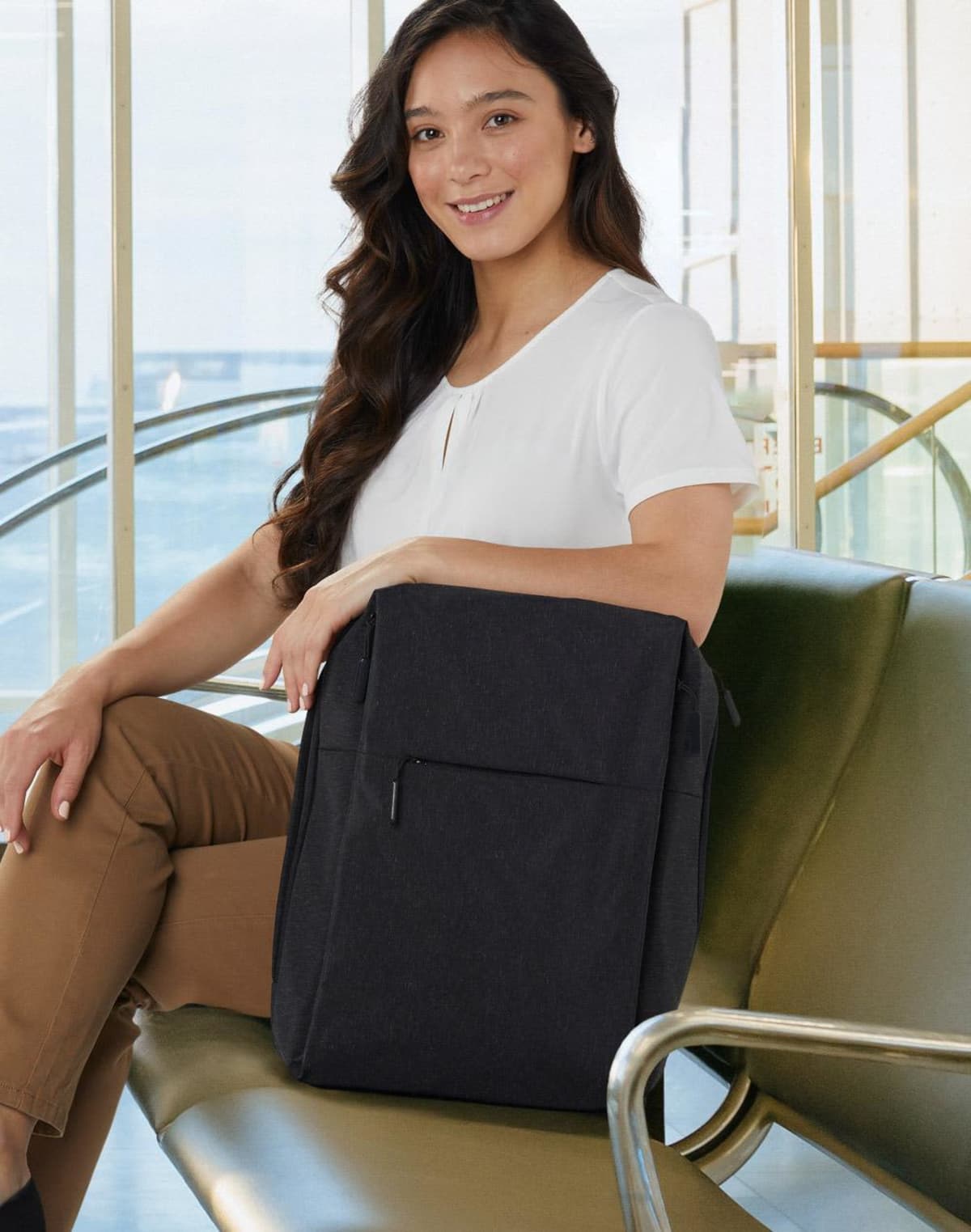 Person sitting on a bench, holding a black backpack, and smiling at the camera.