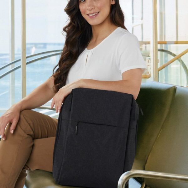 Person sitting on a bench with a black backpack, smiling and wearing a white shirt and tan pants.