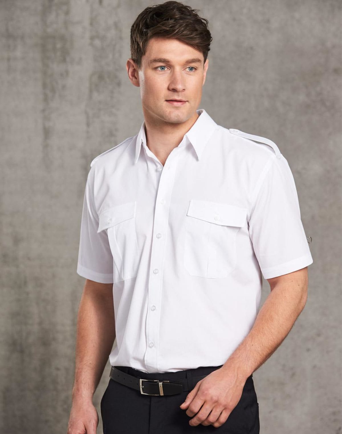 Man wearing a short-sleeve white shirt stands against a gray background.