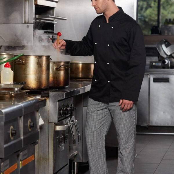 Chef in black uniform stirring a pot on a professional kitchen stove.