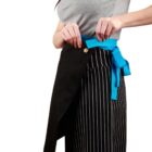 Person in a gray top and striped skirt tying a blue apron around their waist.