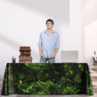 Man standing behind a table with a leafy green tablecloth in a modern office space.