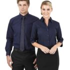 Two people in business attire stand side by side. The person on the left wears a navy shirt with a tie, while the person on the right wears a navy blouse. Both are smiling against a plain white background.