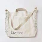 Beige tote bag with bizcare logo and doodle-patterned sides.