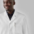 Smiling man in a white lab coat against a gray background.