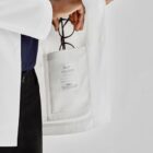 Person holding glasses in the inner pocket of a white lab coat.