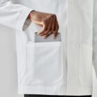 Person in lab coat placing a tablet into a pocket.
