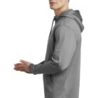 Man in a gray hoodie standing sideways with hands slightly clasped, looking forward.