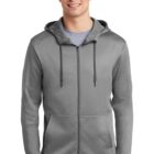 Man wearing a gray zip-up hoodie with front pockets and a hood, standing and smiling.