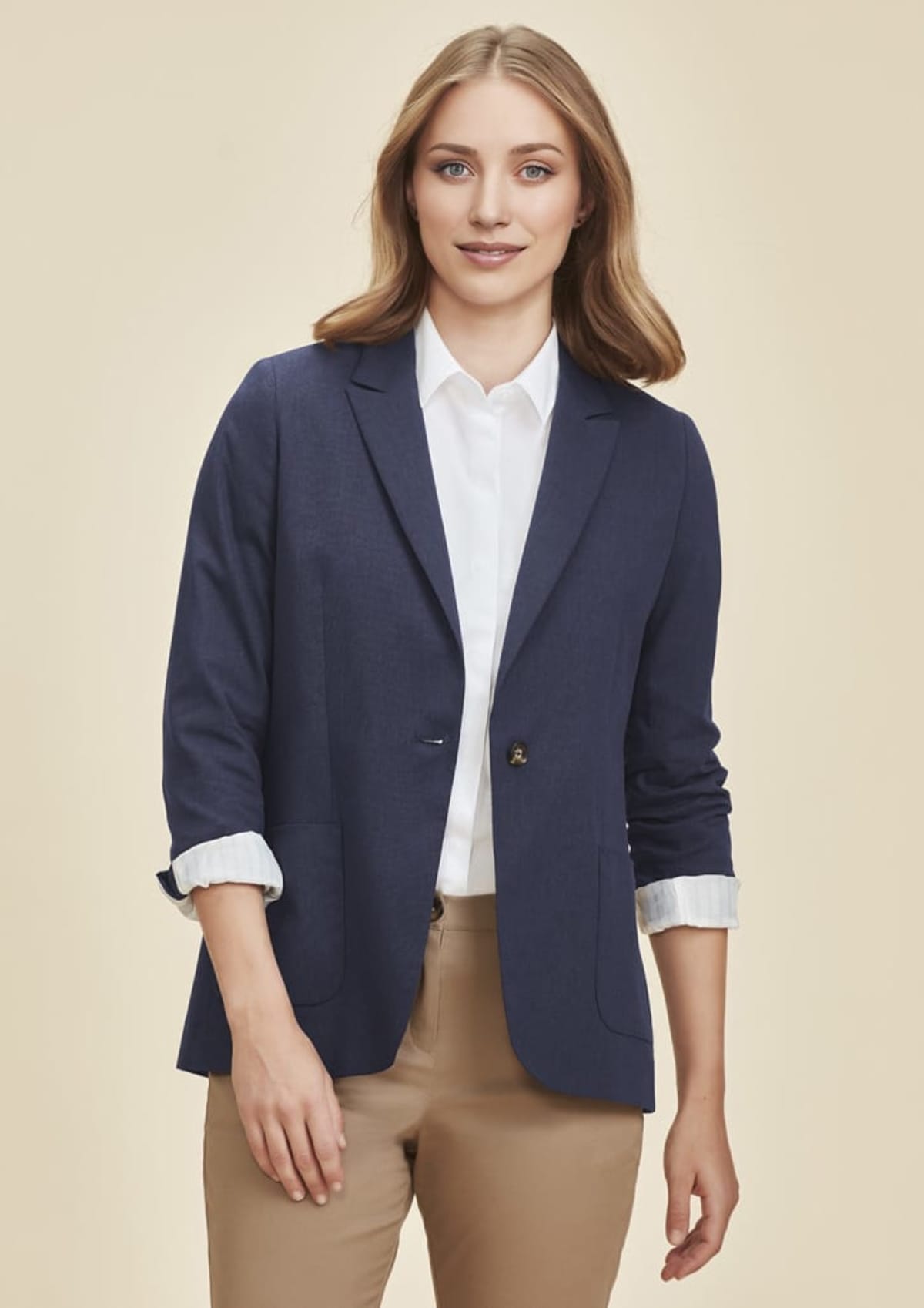 Person wearing a navy blazer, white shirt, and khaki pants against a beige background.