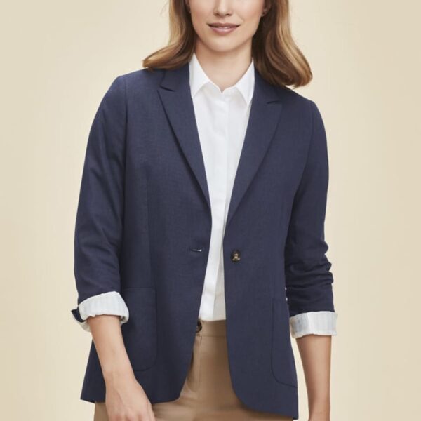 Person in navy blazer, white shirt, and beige pants, standing and smiling.
