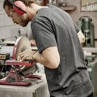 Person with headphones and goggles sanding wood on a disc sander in a workshop.