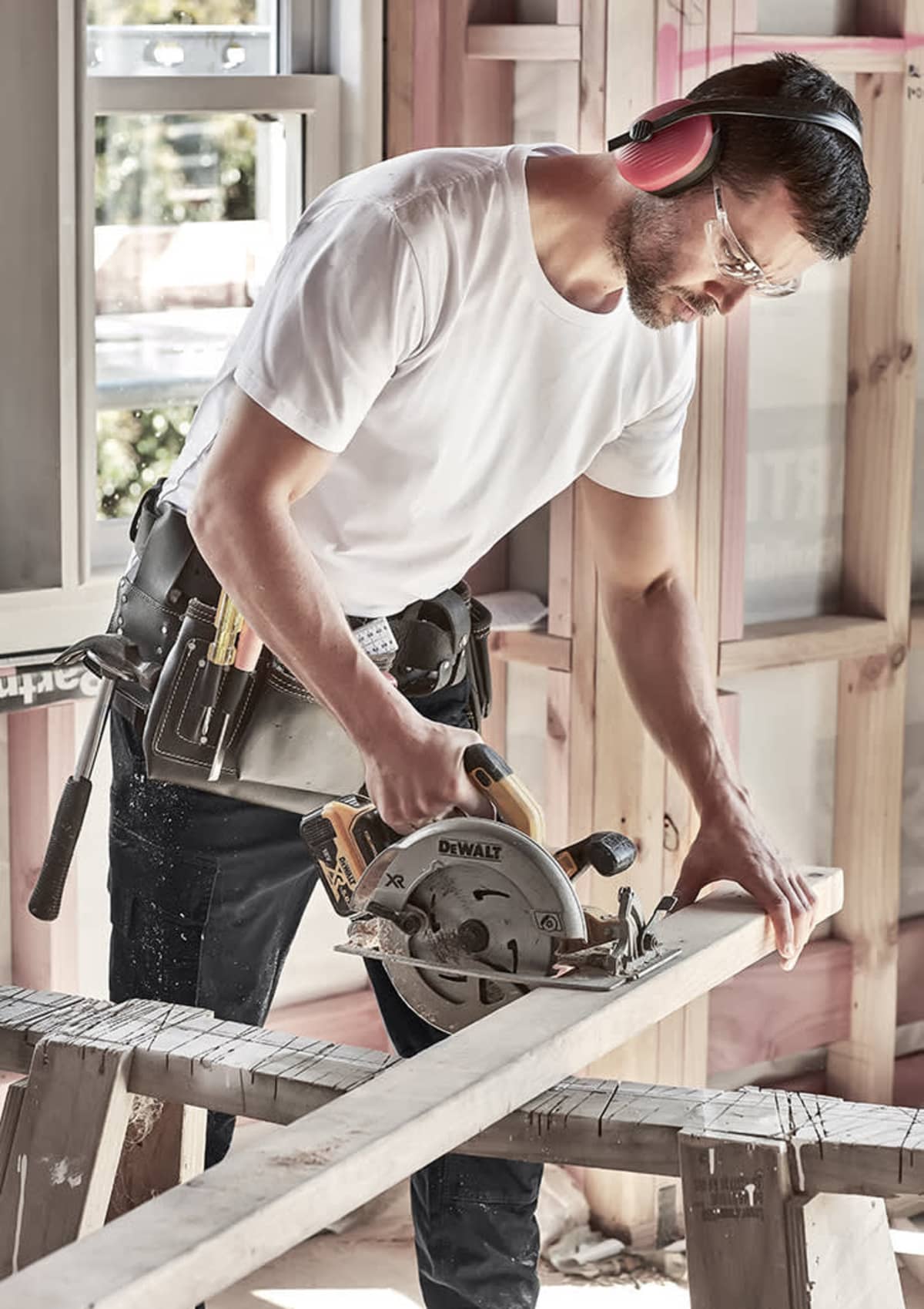 A man using a circular saw to cut wood, wearing safety glasses and earmuffs.
