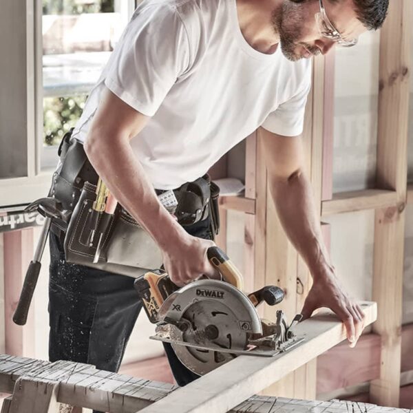Carpenter wearing ear protection cutting wood with a circular saw in a workshop.