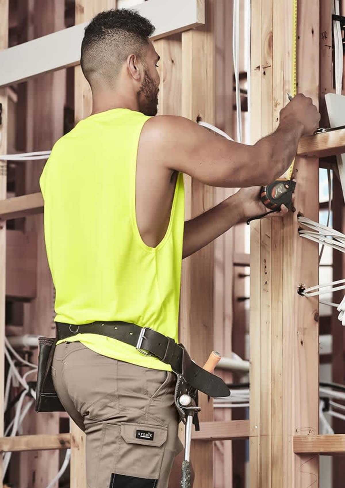 A construction worker measures wood beams at a building site.