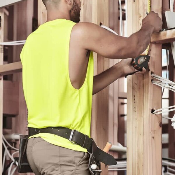 Man in a neon yellow tank top measures wood framing at a construction site.
