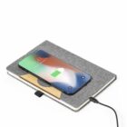 A smartphone charging wirelessly on top of a closed gray notebook connected by a cable.
