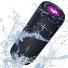 A black cylindrical Bluetooth speaker with a pink logo and white control buttons is shown with water splashing around it, highlighting its water-resistant feature.