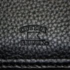 Close-up of a textured black leather surface with the Cutter & Buck logo embossed in the center. The pattern exhibits a pebbled texture, highlighting the brands signature style.