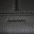 Close-up of black leather with visible texture. The words Genuine Leather are embossed in the center. Stitching is also visible, dividing the surface into sections.