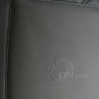 Close-up of a dark binder or folder with the embossed logo CBH GROUP featuring a circular design of small, raised dots. The material appears sleek and textured, with a fabric edge visible on the left.