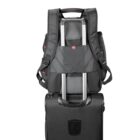 A black backpack is securely attached to the extended handle of a rolling suitcase. The suitcase is black, and the setup is viewed from the back, suggesting a travel-ready configuration.
