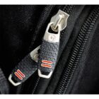 Close-up of two interlocked black and silver zipper pulls with textured grips and red stripes on a black fabric background. The zippers are slightly open, revealing part of the zipper teeth.