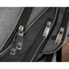 Close-up of a gray backpack featuring multiple zippered compartments. The zippers, with metal pulls, are prominently displayed. The fabric has a textured appearance, and part of a brick wall is visible in the background.