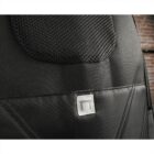 Close-up of a black backpack showing a textured mesh padding and a small square logo with a geometric design. The fabric appears durable, and the stitching is visible, indicating quality craftsmanship. The background is slightly blurred.