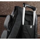 Close-up of a gray fabric backpack with an extendable handle, similar to a suitcase. The bag is leaning against a red brick wall, showcasing its zippered compartments and quilted back panel.