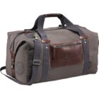 A gray duffel bag with dark brown leather accents and handles. It features a front zippered pocket, side pocket with a round patch, and black shoulder strap with silver hardware.