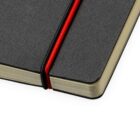 A close-up of a black notebook partially open on a white surface. A red elastic band bookmarks the pages, and the edges of the pages appear slightly worn. The cover has a textured appearance.