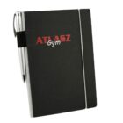A black notebook with ATLASZ Gym in red and white on the cover. A silver pen is attached to the side with an elastic holder. An elastic band secures the notebook closed.